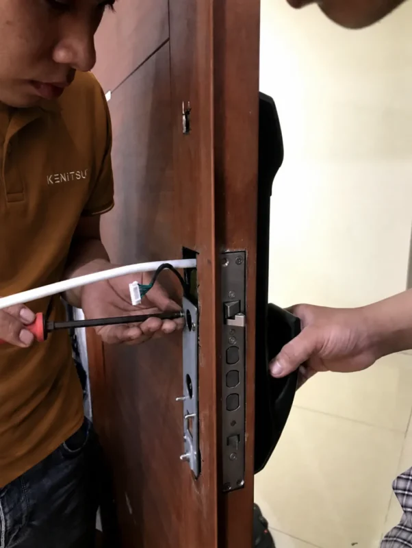 Kỹ thuật viên Kenitsu lắp thân khóa vân tay trên cửa gỗ căn hộ