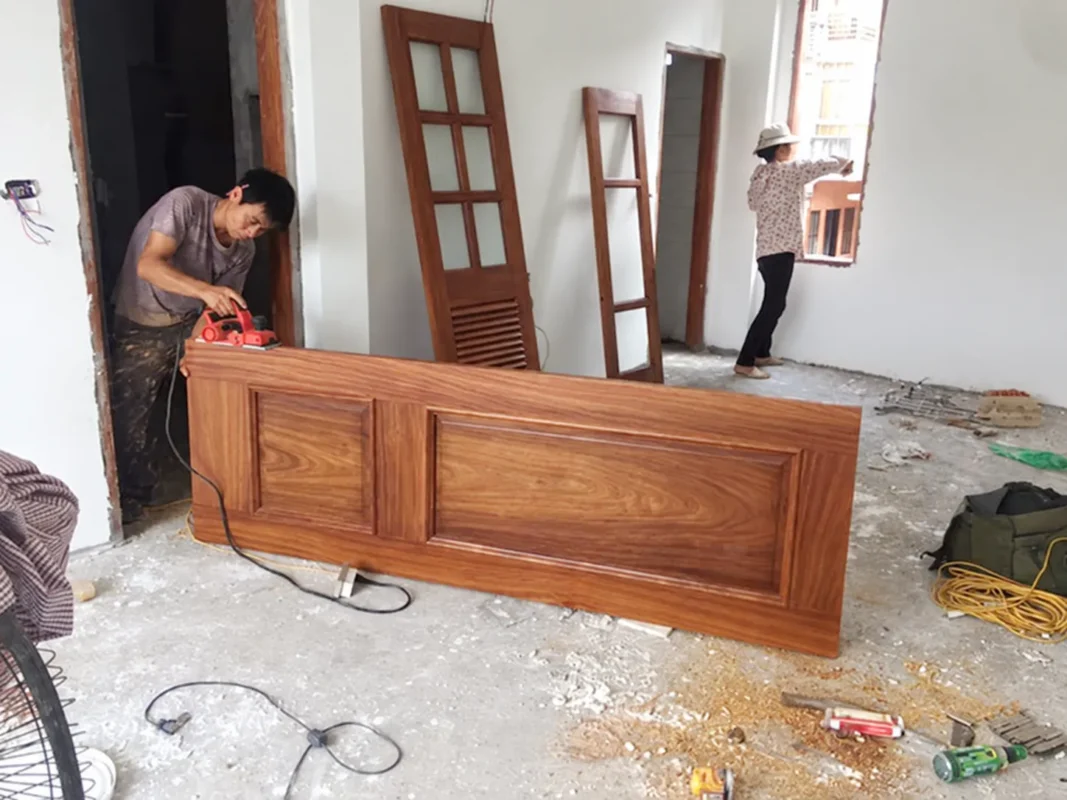 Lắp khóa vân tay khi nào? Trước hay sau khi làm nội thất? 2 Thợ dùng máy bào chỉnh cạnh cánh cửa gỗ tại công trình đang hoàn thiện.