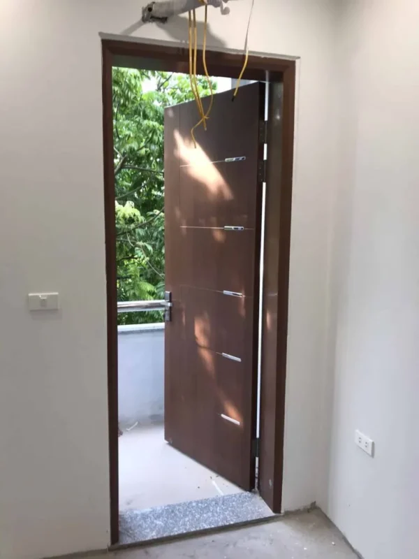 Cửa một cánh màu nâu mở ra ngoài, đang lắp khóa cơ tay gạt.