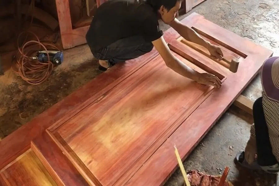 Lắp khóa vân tay khi nào? Trước hay sau khi làm nội thất? 3 Thợ dùng búa cao su chỉnh chi tiết trên cánh cửa gỗ đặt nằm ngang.