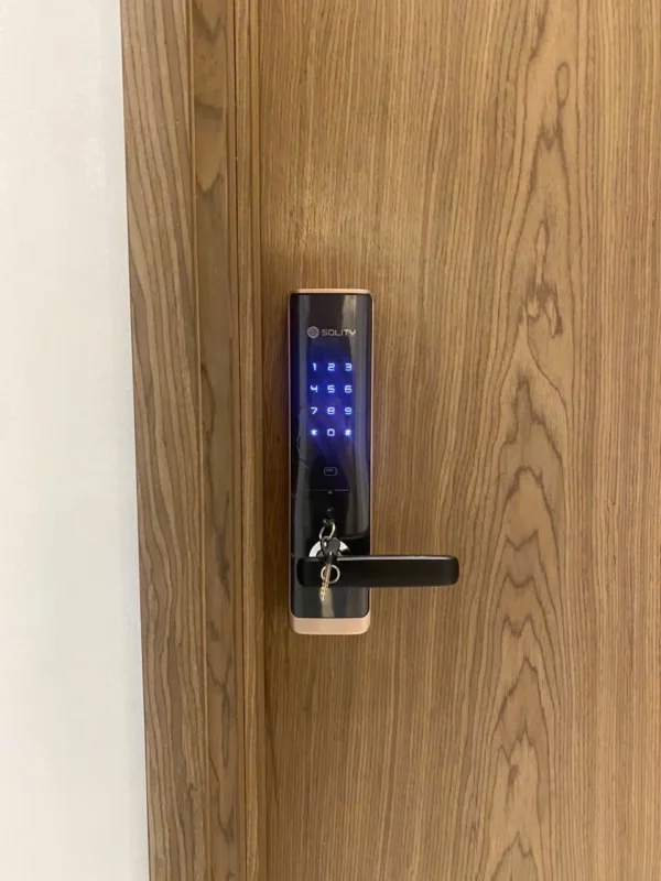 Khóa Solity GM-7000BK trên cửa gỗ với bàn phím sáng xanh và chìa cơ cắm ở mặt ngoài.